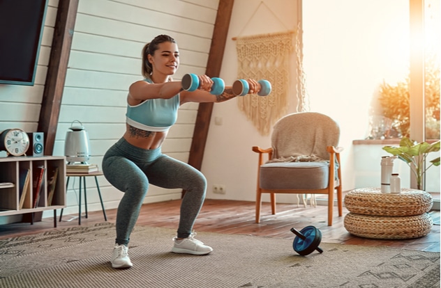 athletic girl in leggings and top crouches with dumbbells at home.